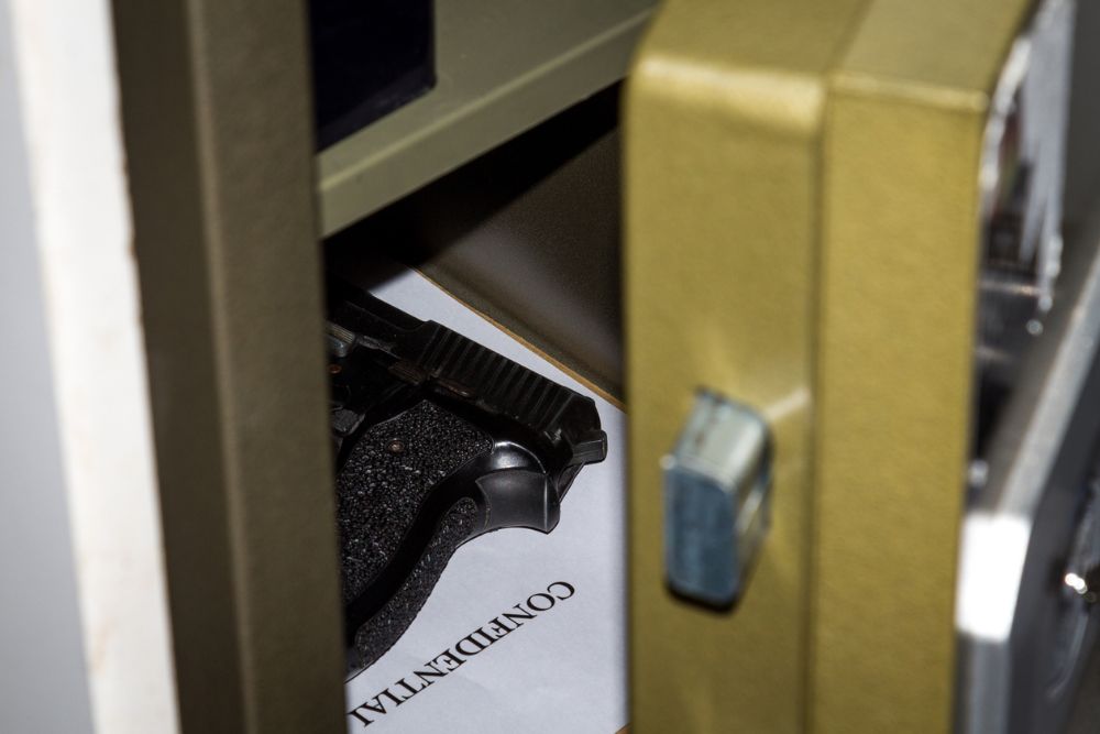 Gun stored inside an open safe on top of a document labeled “Confidential.”