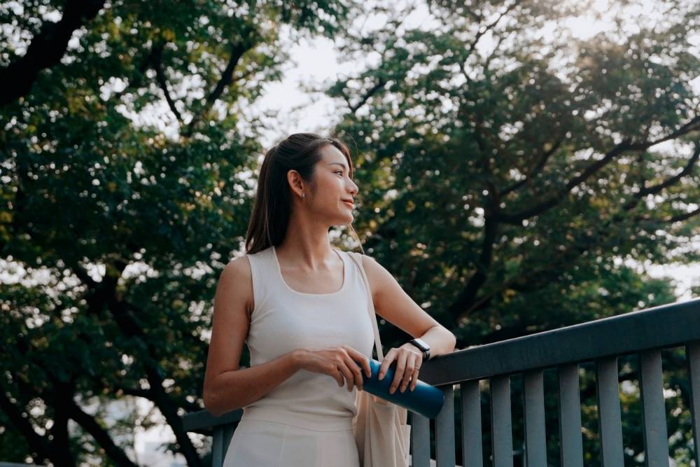 Woman standing outdoors on a bridge, holding a water bottle and gazing into the distance