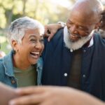 A joyful group of older adults laughing and embracing outdoors, sharing a warm moment of connection and friendship.