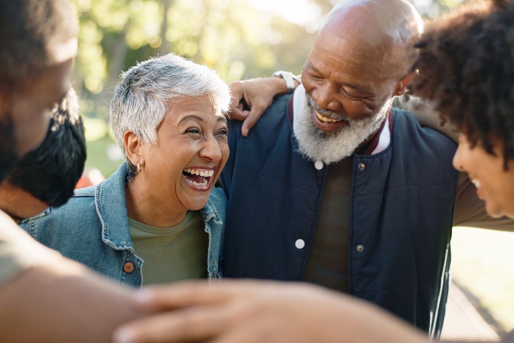A joyful group of older adults laughing and embracing outdoors, sharing a warm moment of connection and friendship.