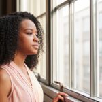 portrait of a young woman looking out a window pensively - tips to manage anxiety - self-care to manage anxiety