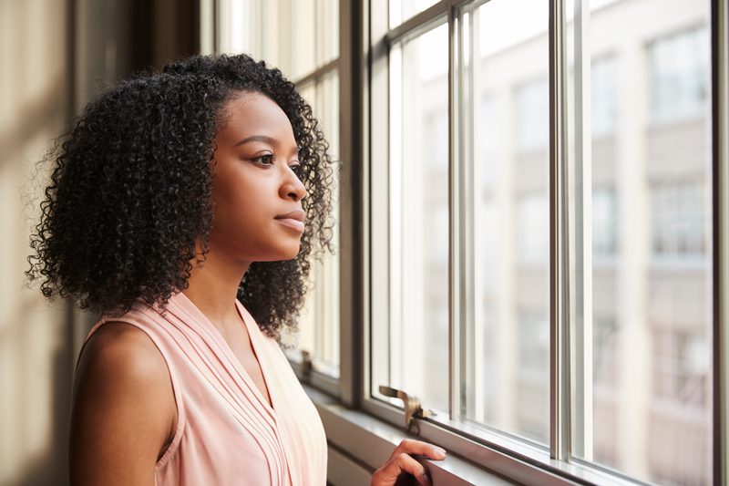 portrait of a young woman looking out a window pensively - tips to manage anxiety - self-care to manage anxiety