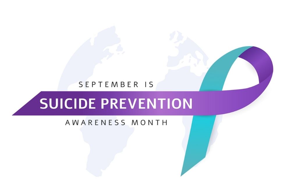 Purple and teal awareness ribbon with text that reads ‘September is Suicide Prevention Awareness Month’ on a light background.