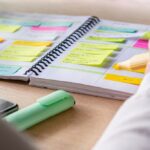 A person highlights notes in a colorful planner filled with sticky notes and schedules, symbolizing structure, routine, and organization.